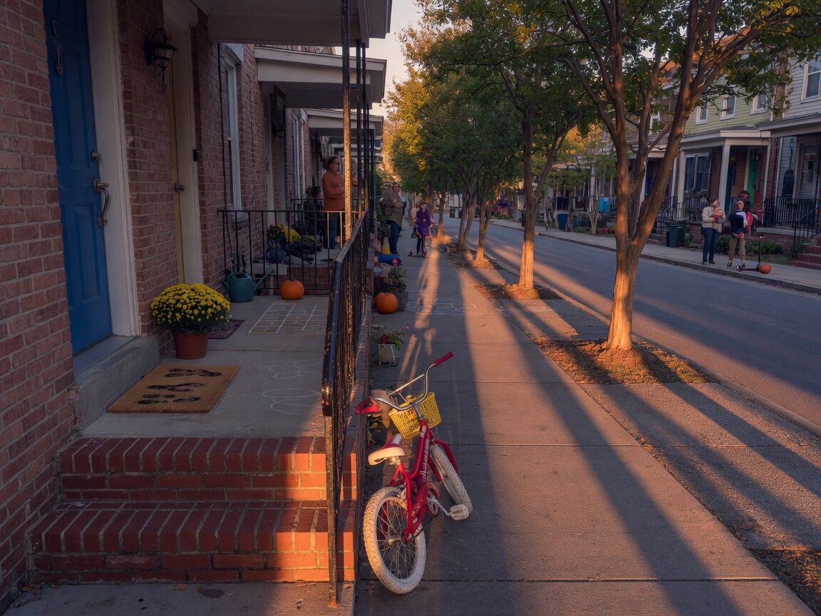 A townhome porch at golden hour, a bicycle against the brick railing.